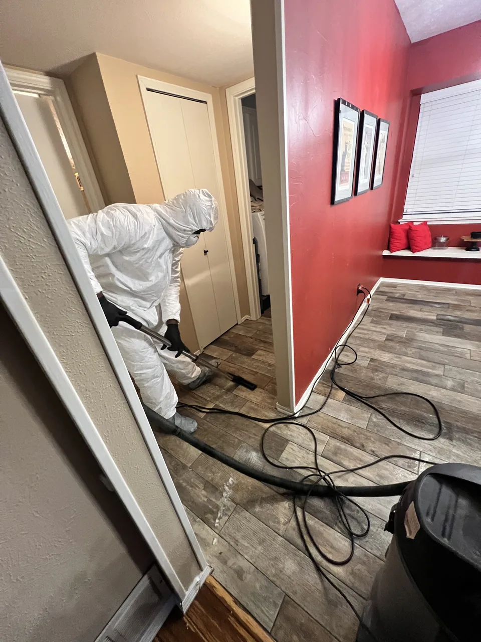 Technician in protective coveralls using floor-cleanup equipment inside a residence